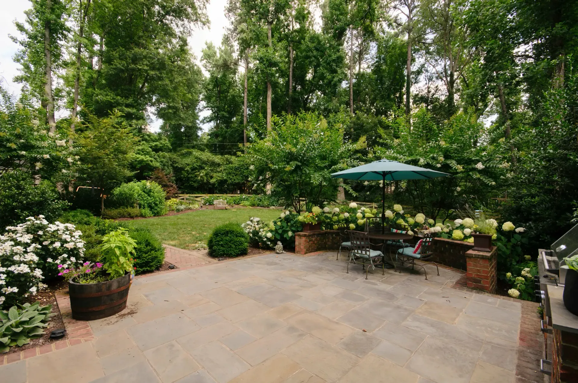 Patio garden with potted plants, trees, and a small table under a green umbrella