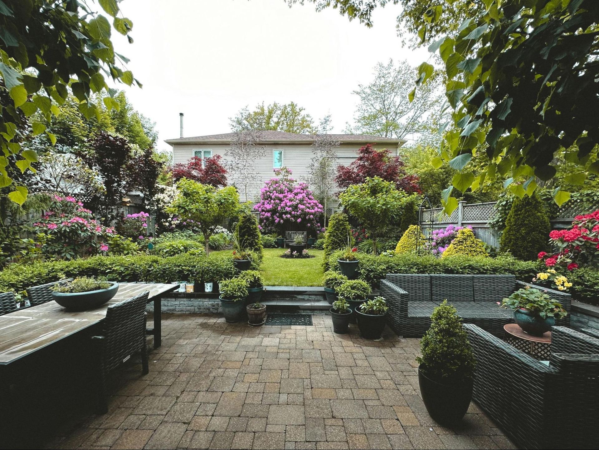 Lush garden patio with stone paving, benches, and blooming pink flowers around a small water feature