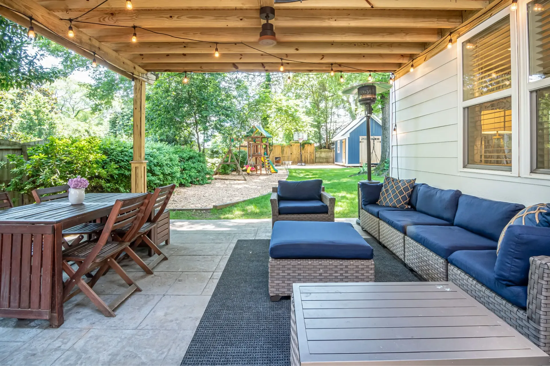 Covered patio with blue outdoor sofa, dining table, and backyard greenery