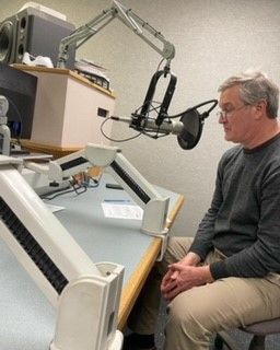 A man is sitting at a desk in front of a microphone.
