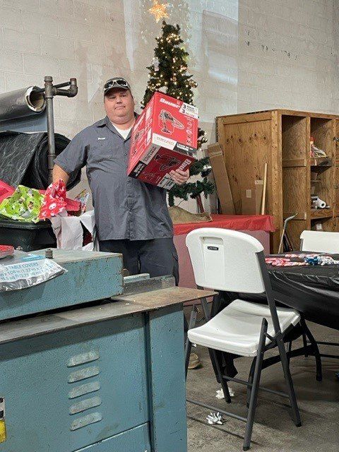 A man is holding a box in front of a christmas tree.