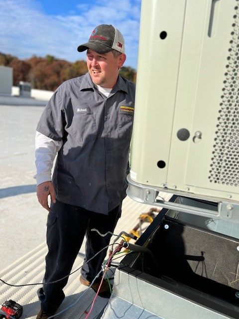 A man in a hat is standing next to an air conditioner on a roof.