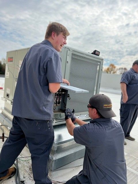 Two men are working on an air conditioner on a roof