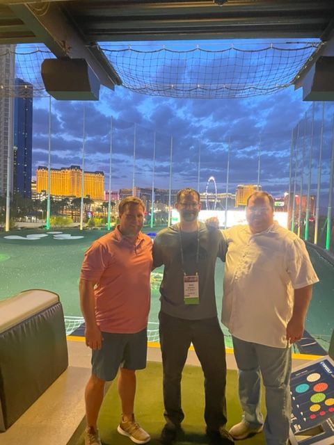 Three men are posing for a picture in front of a golf course.
