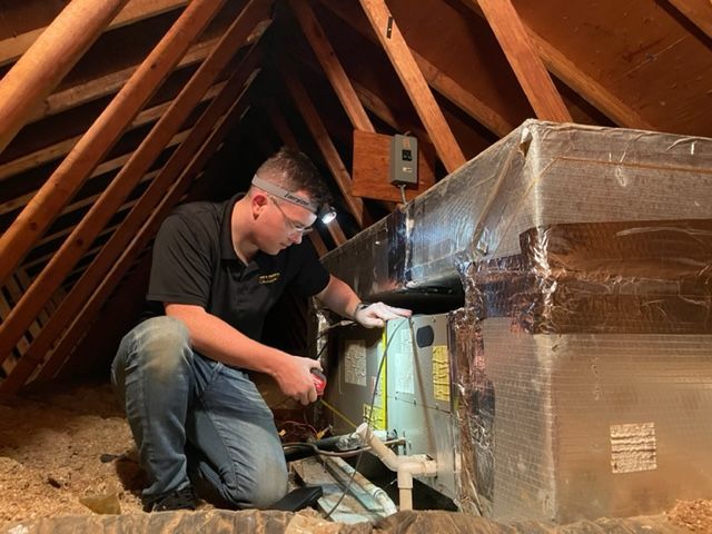 A man is working on an air conditioner in an attic.