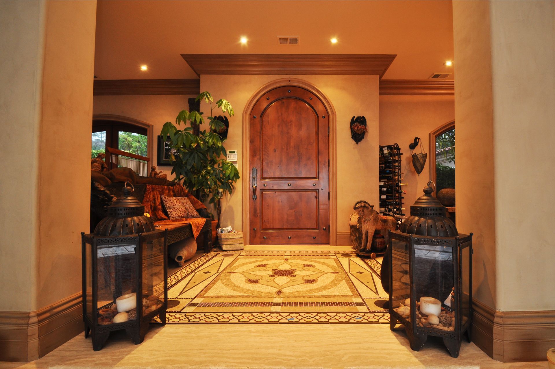 An ornate wooden front door in a luxurious entryway. Features include stone tile flooring, decorative lanterns, and warm lighting.