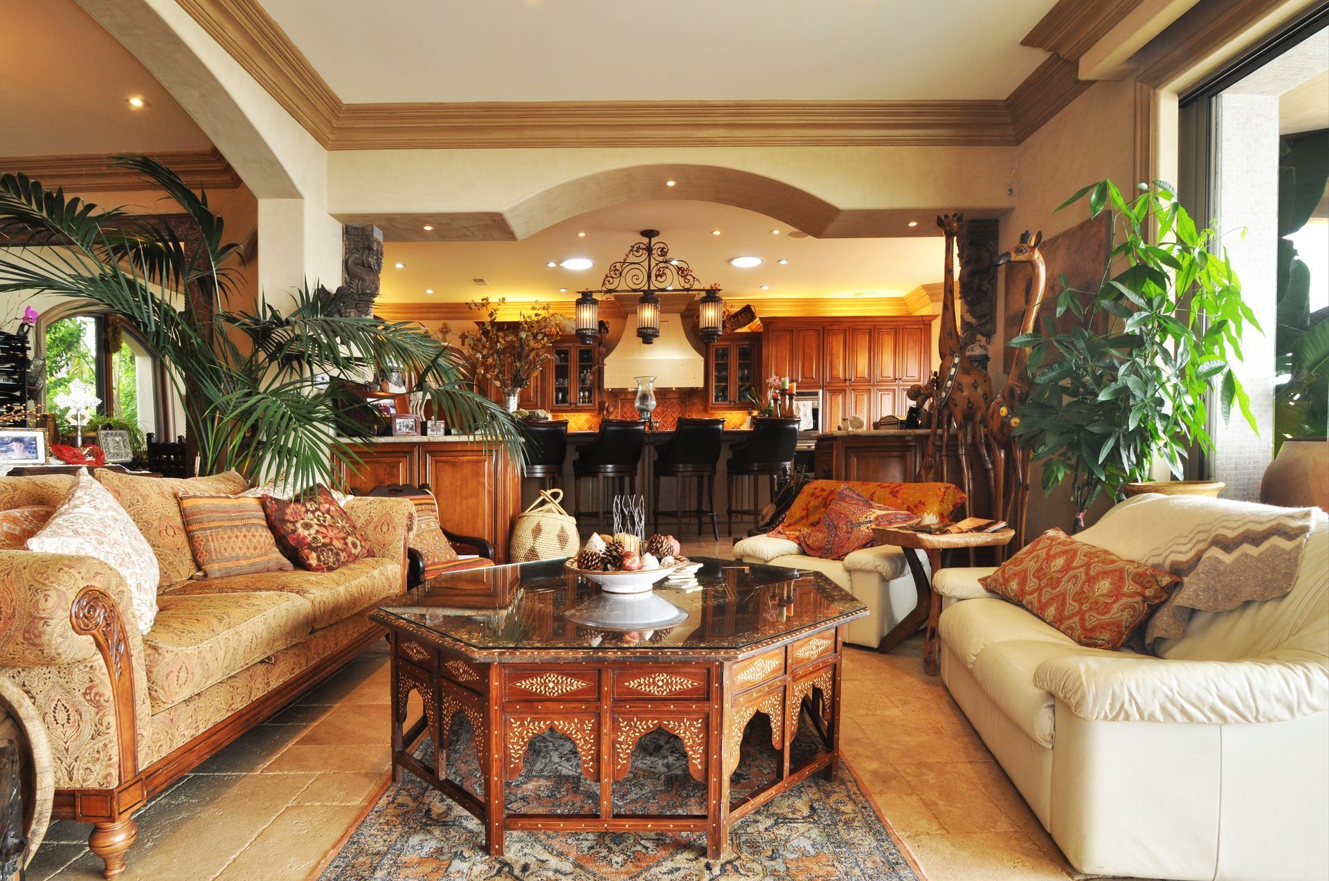 Living room with ornate furniture, plants, and a view into a kitchen with a bar.