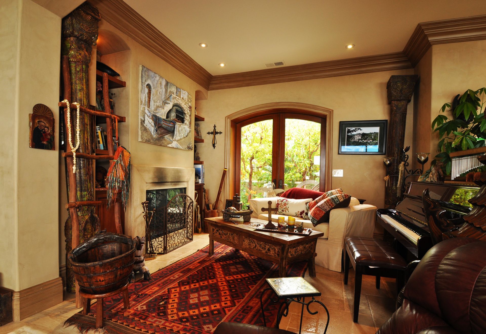 Cozy living room with fireplace, piano, and ornate wooden furniture, featuring a window overlooking greenery.