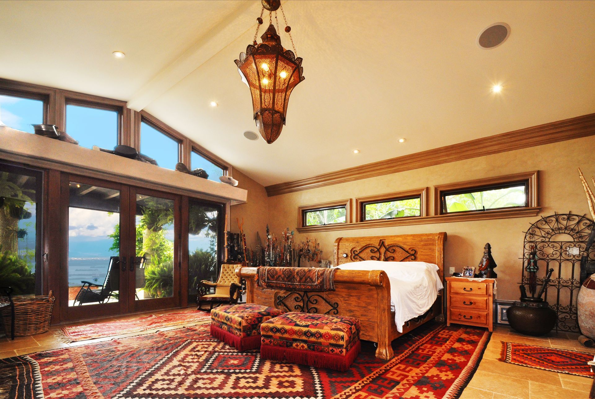 Spacious bedroom with large bed, oriental rug, ornate light fixture, and windows with an outdoor view.