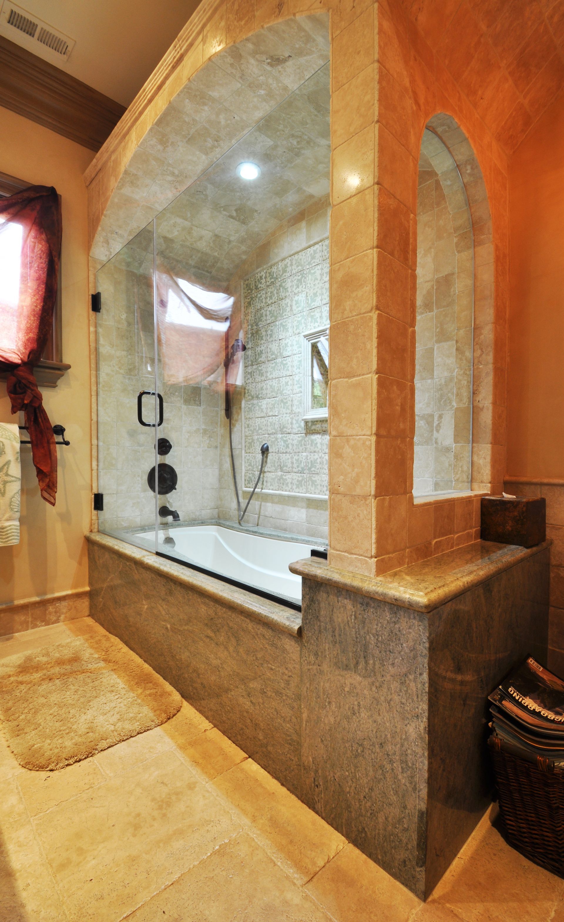 Bathroom with a tiled tub and shower area framed by arches. Beige and orange hues dominate.