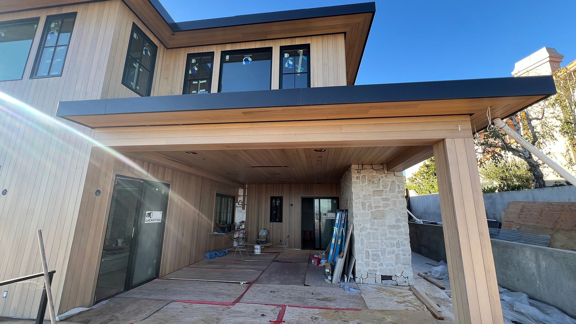 Exterior view of a house under construction with wood siding, a covered patio area, and black trim.