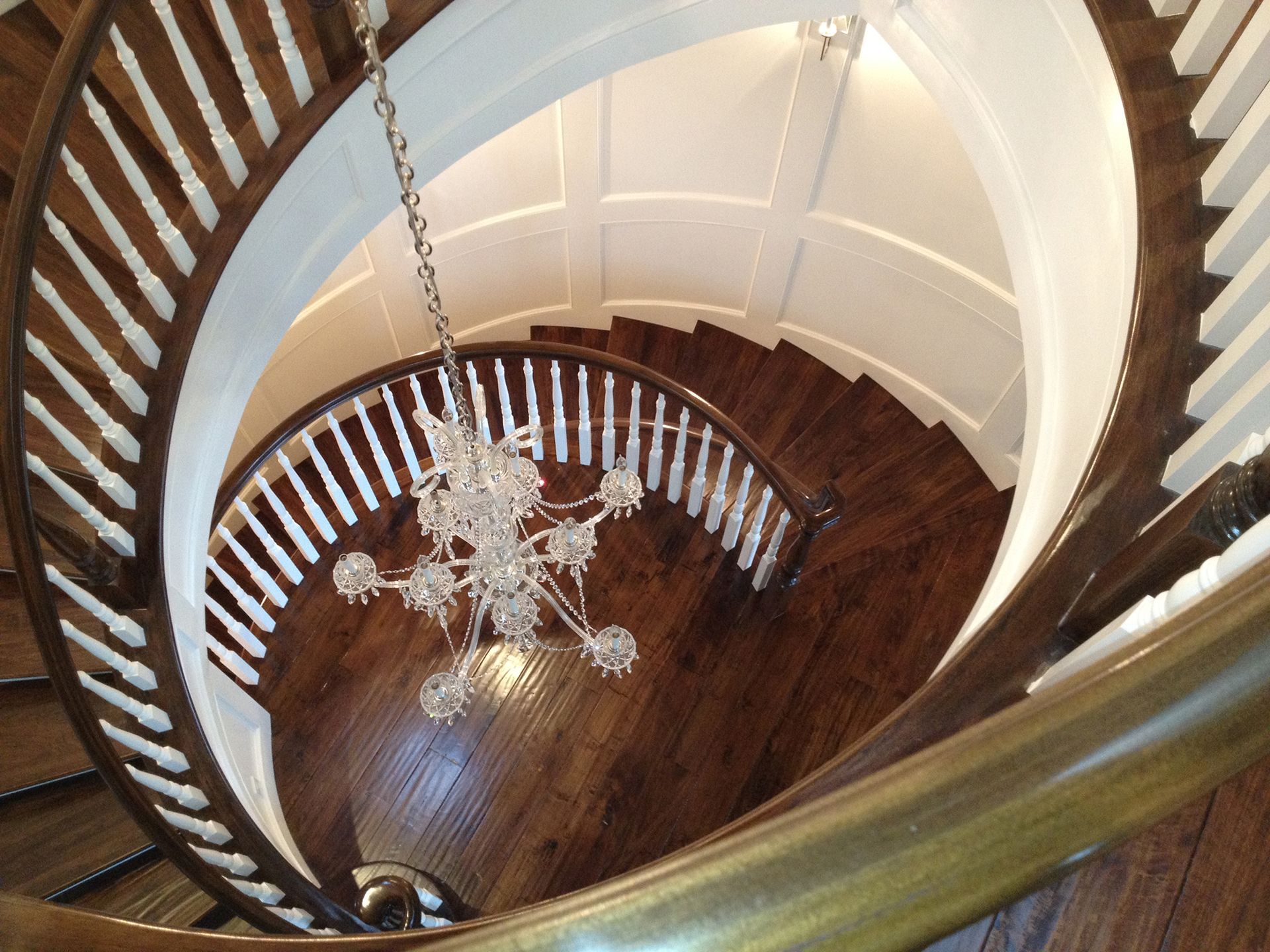 Spiral staircase with wooden steps, white railings, and a hanging chandelier.