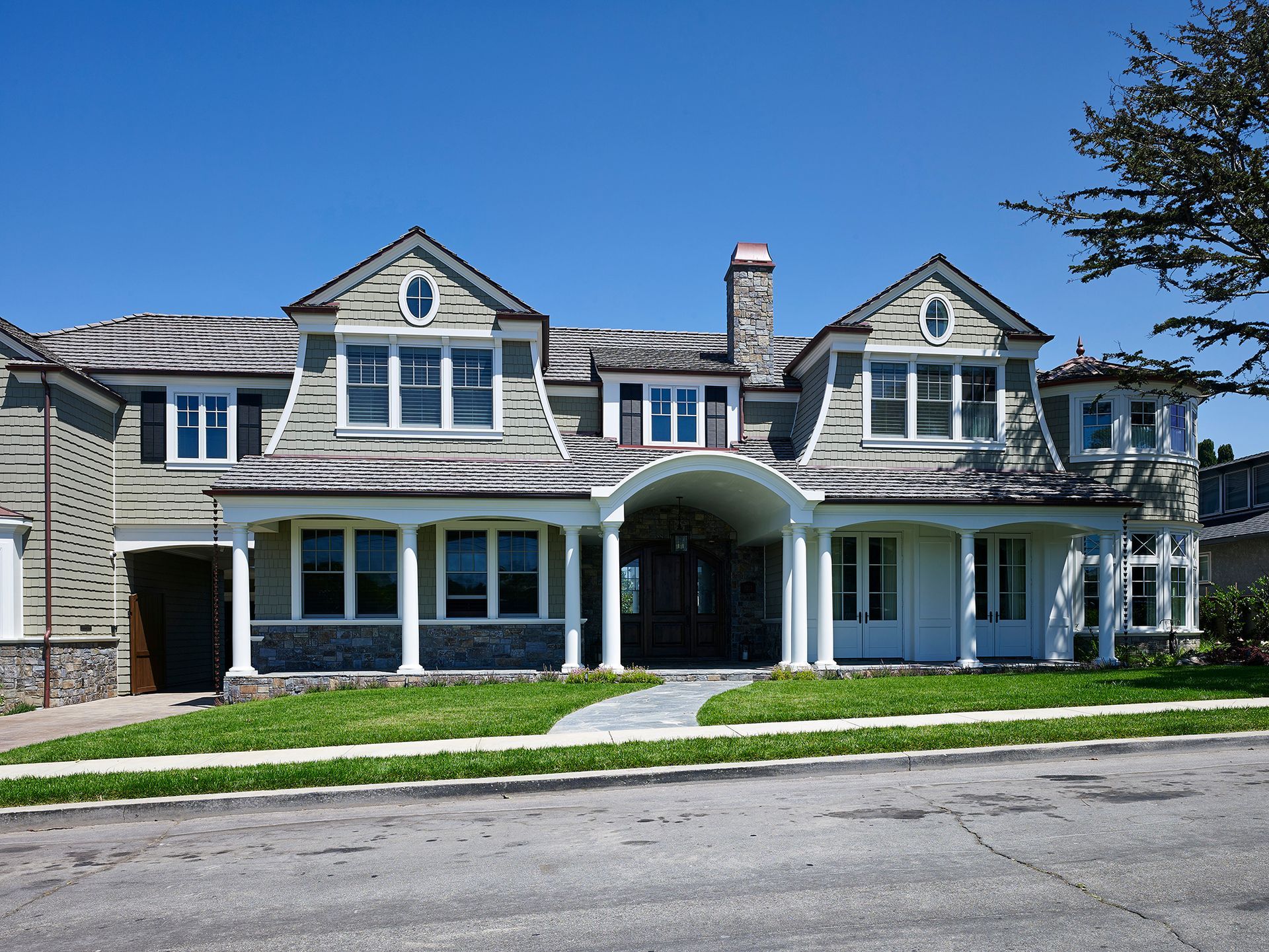Gray and white multi-story house with gabled roof, blue sky, and green grass.