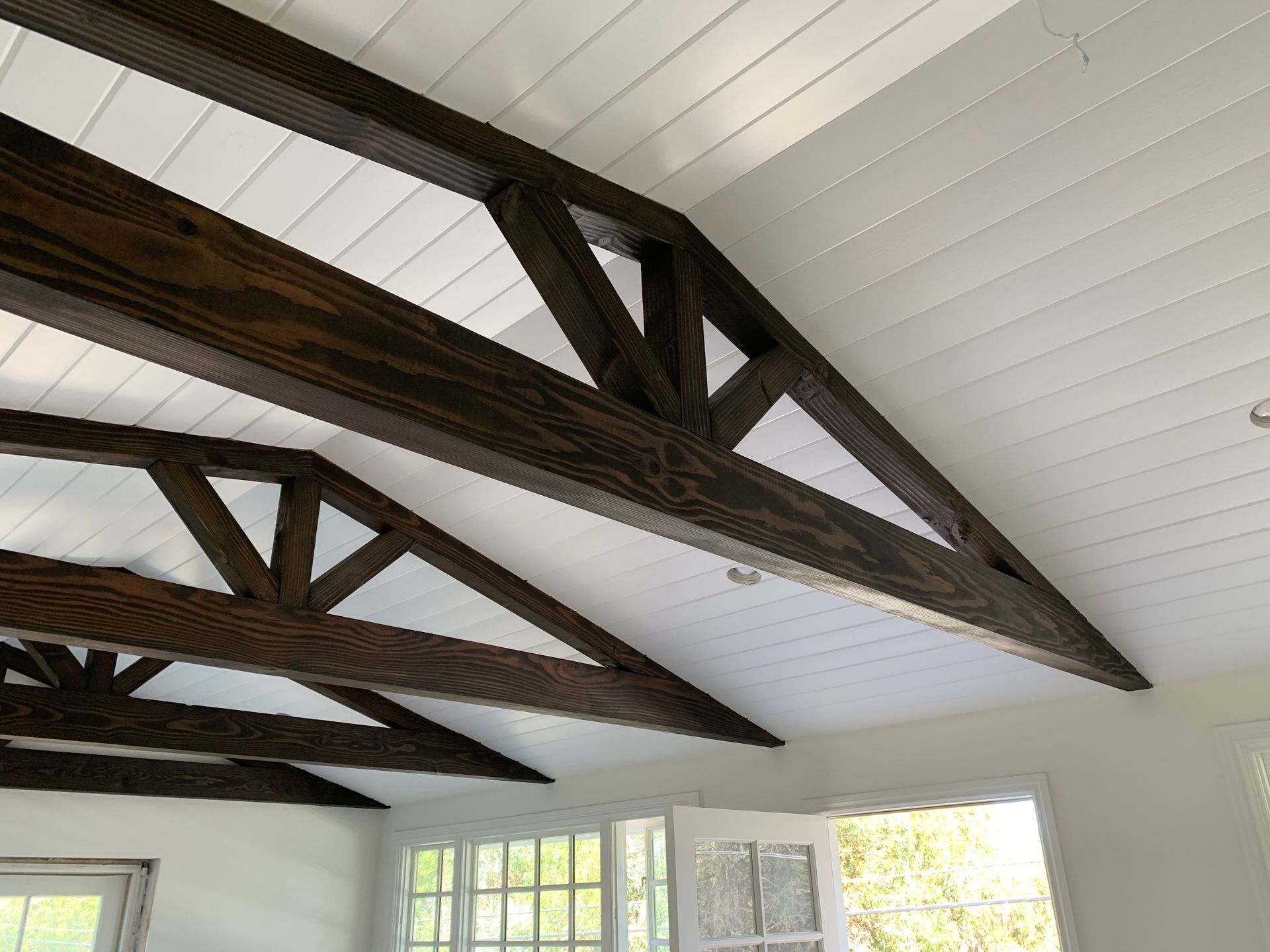 Dark stained wooden beams forming a triangular truss ceiling against a white planked ceiling.