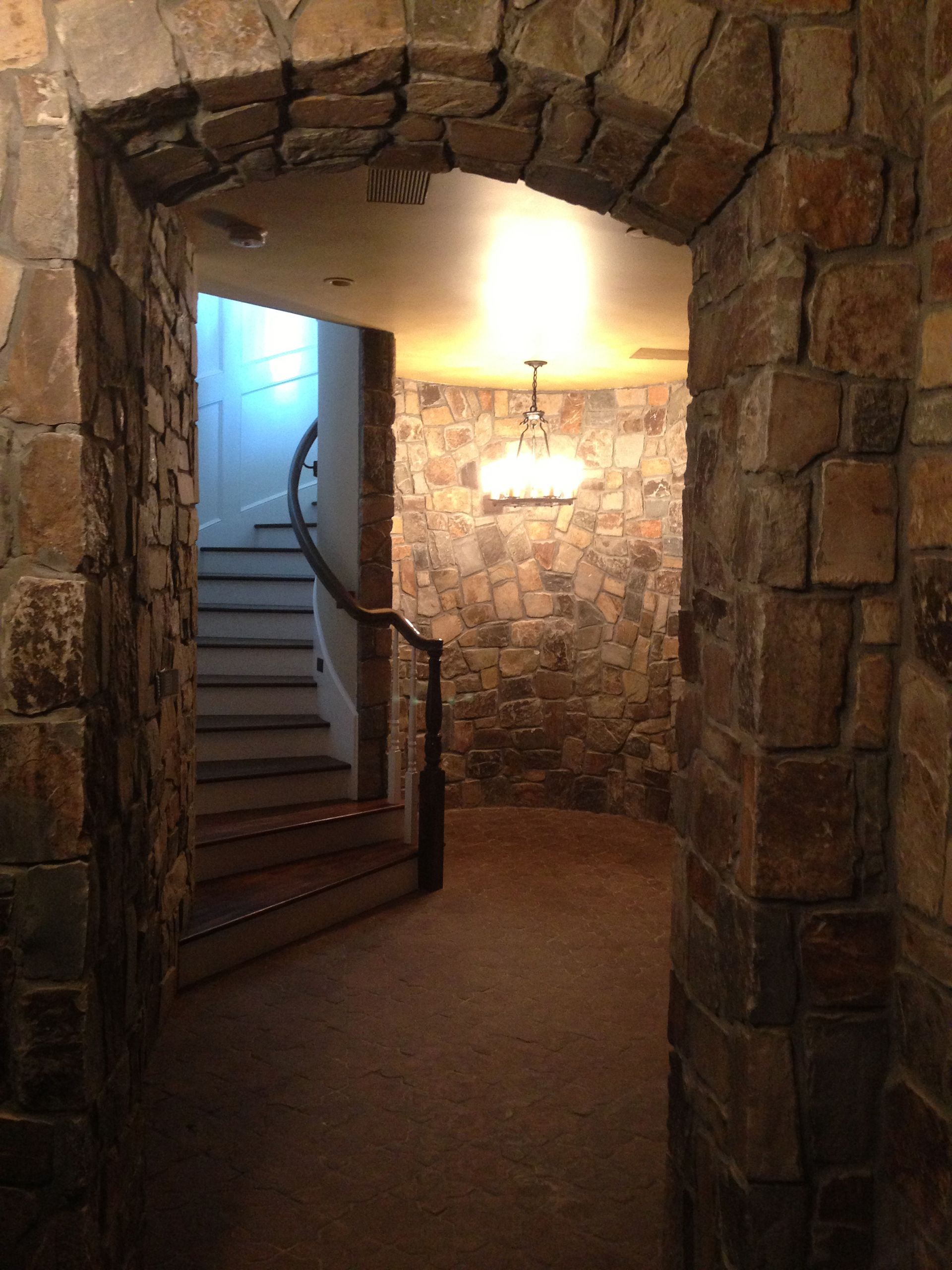 Stone archway leads to room with stone walls, carpet, and stairs to the left.