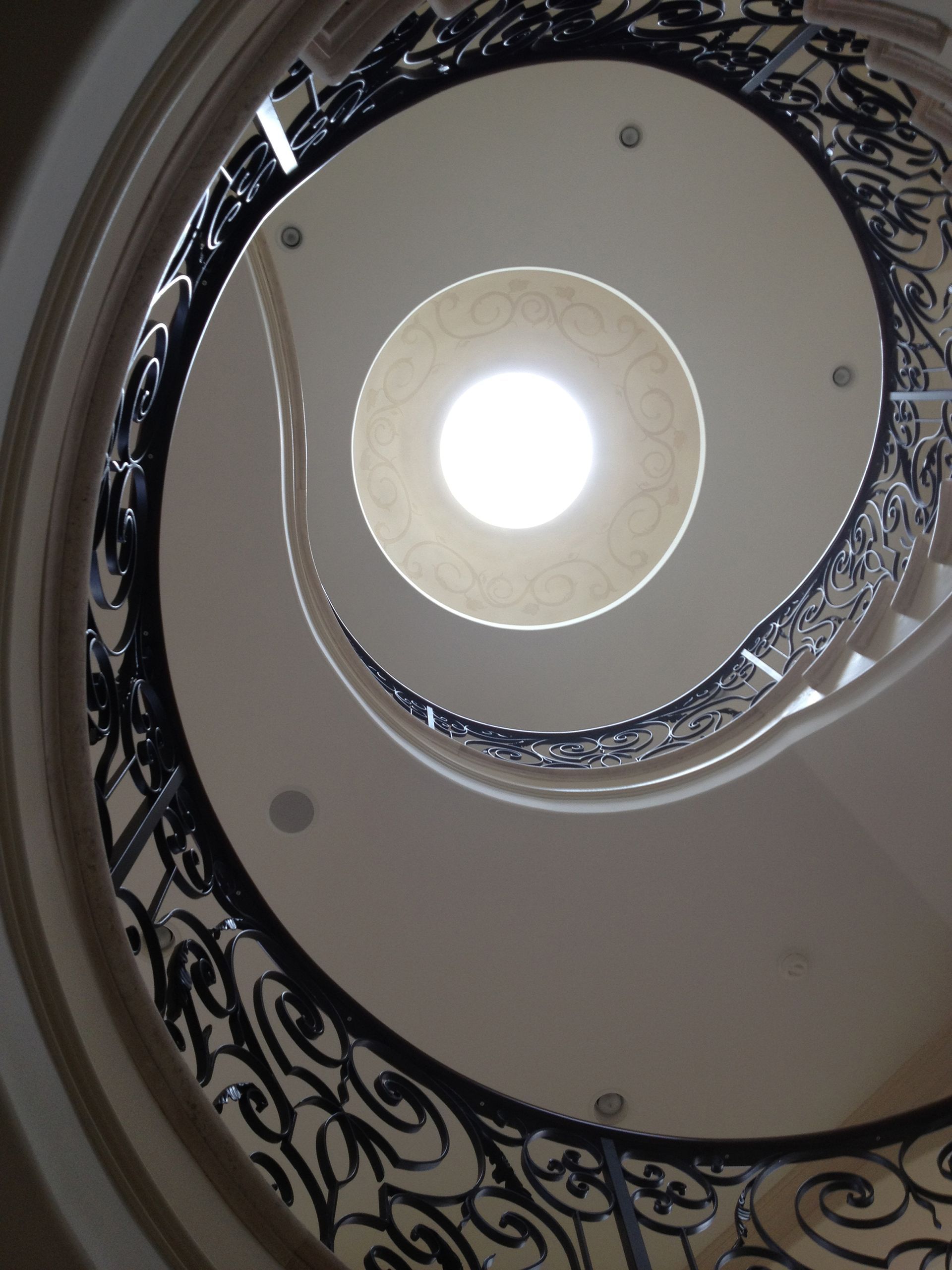 Spiral staircase, wrought iron railing, white walls, looking up to a circular skylight.