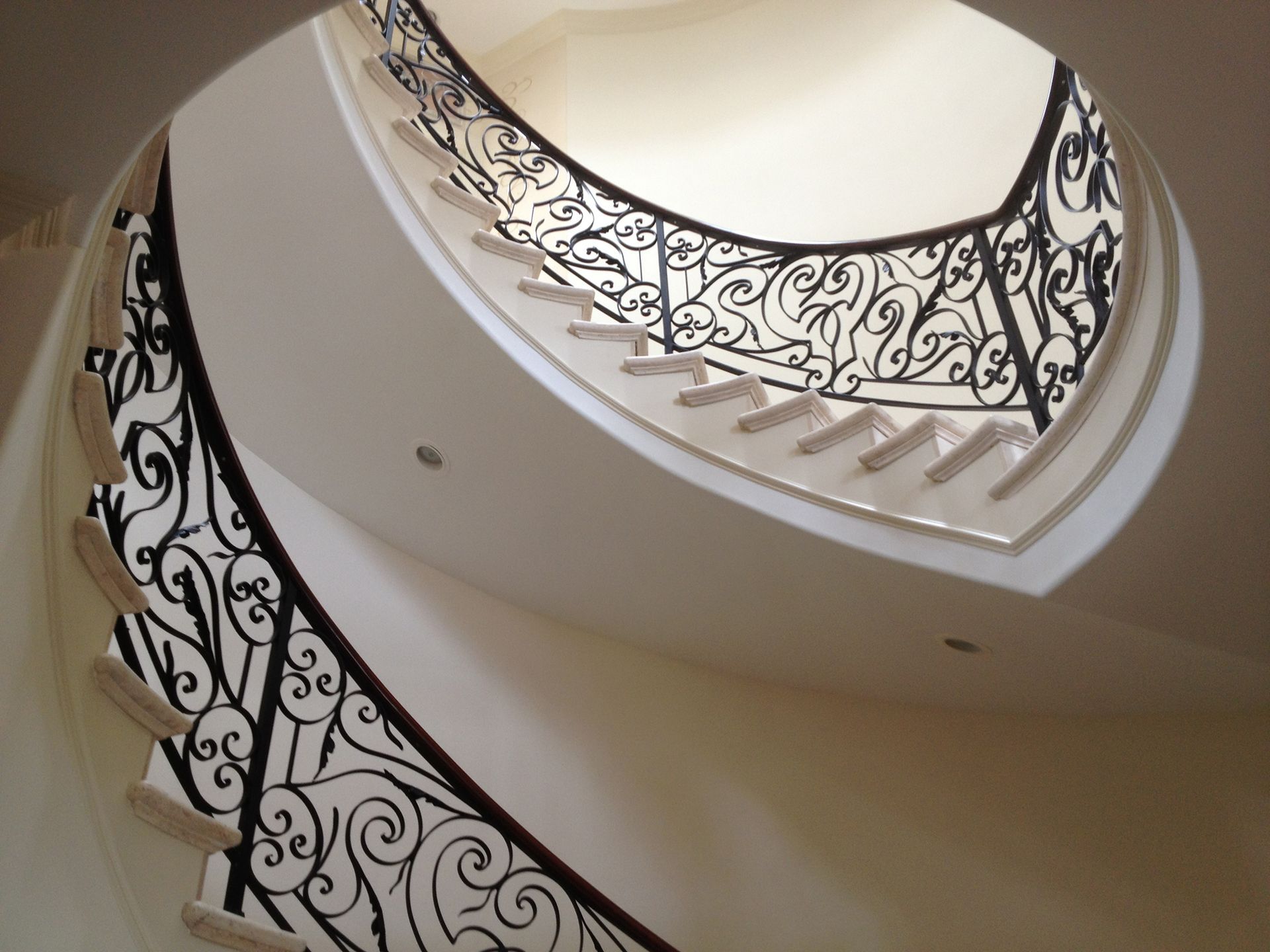 Spiral staircase with ornate black iron railing against a light-colored wall.