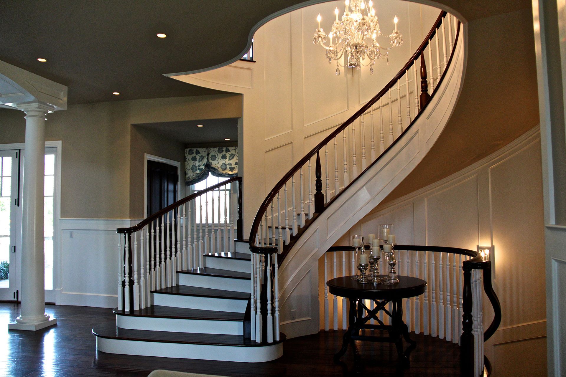 Elegant curved staircase with black banister, white trim, and a chandelier.