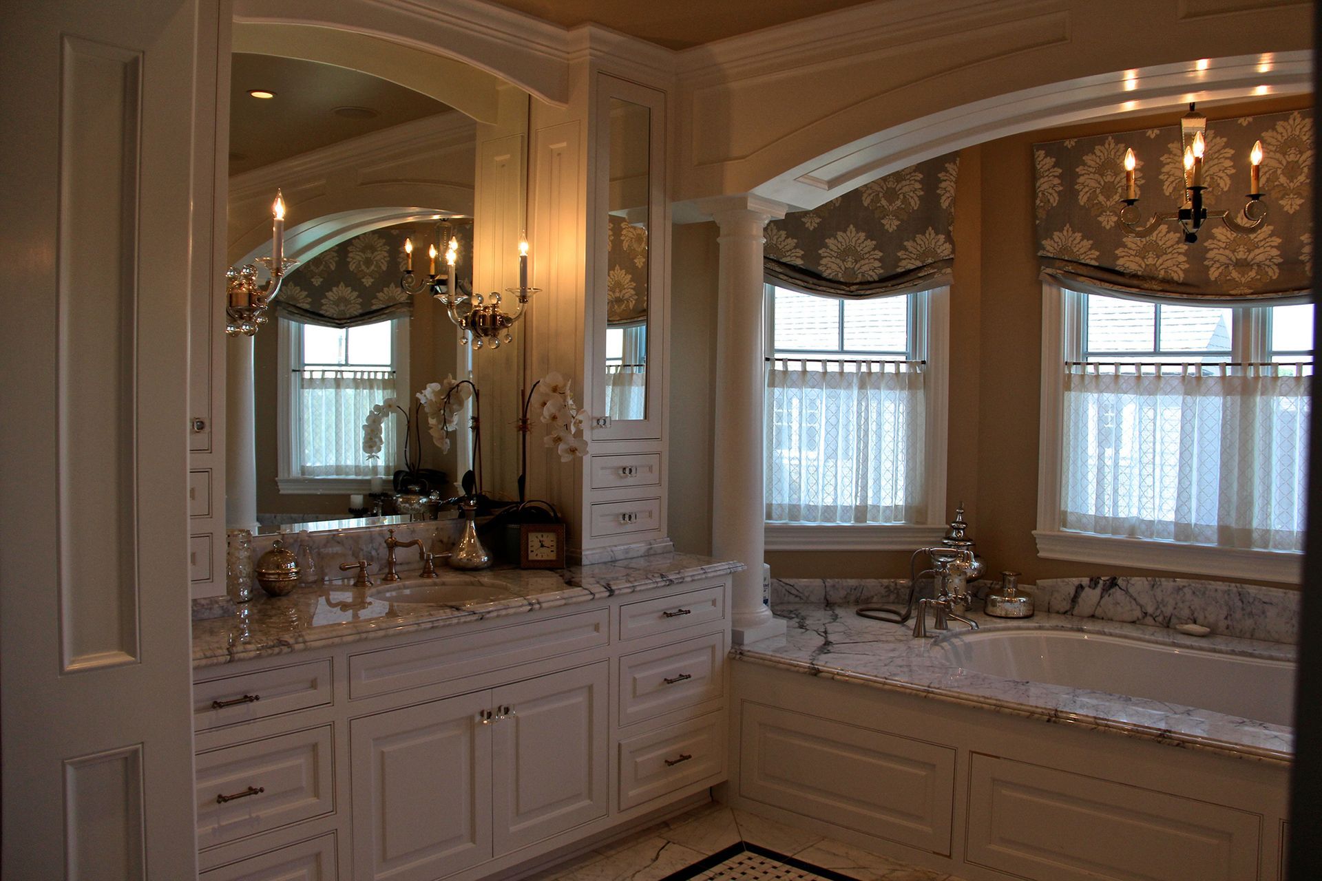Elegant white bathroom with marble countertop, cabinets, large mirror, and soaking tub.