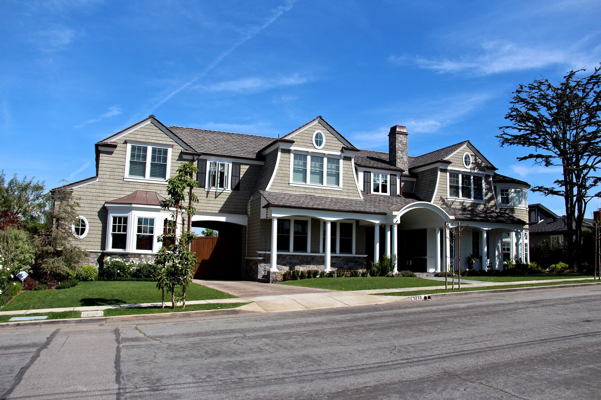 Large two-story house with gray roof and siding, white trim, and a small front yard. Sunny day.