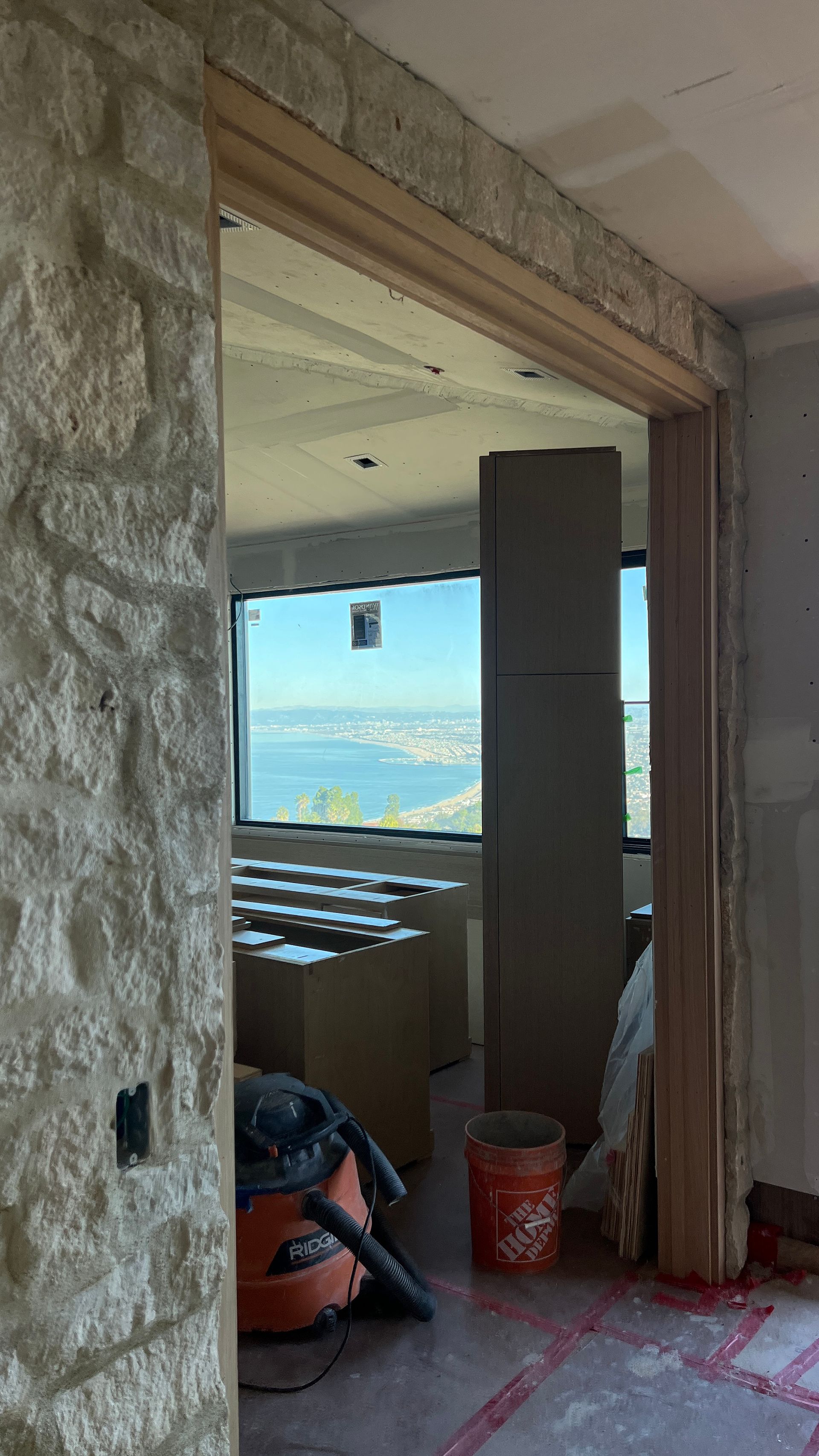 View through a doorway with stone wall, construction in progress, city and water view visible through window.
