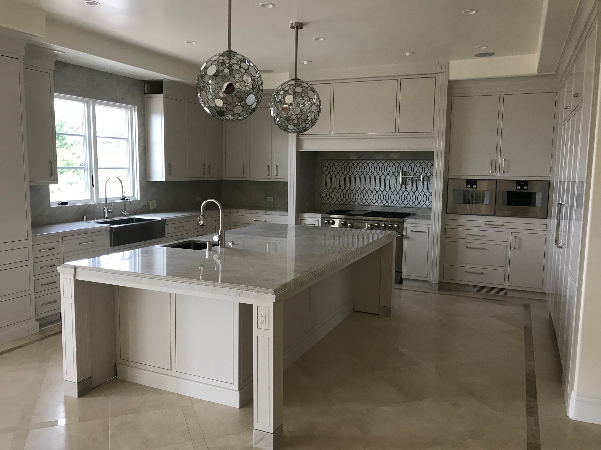 Modern kitchen with gray cabinets, large island, stainless steel appliances, and marble countertops.