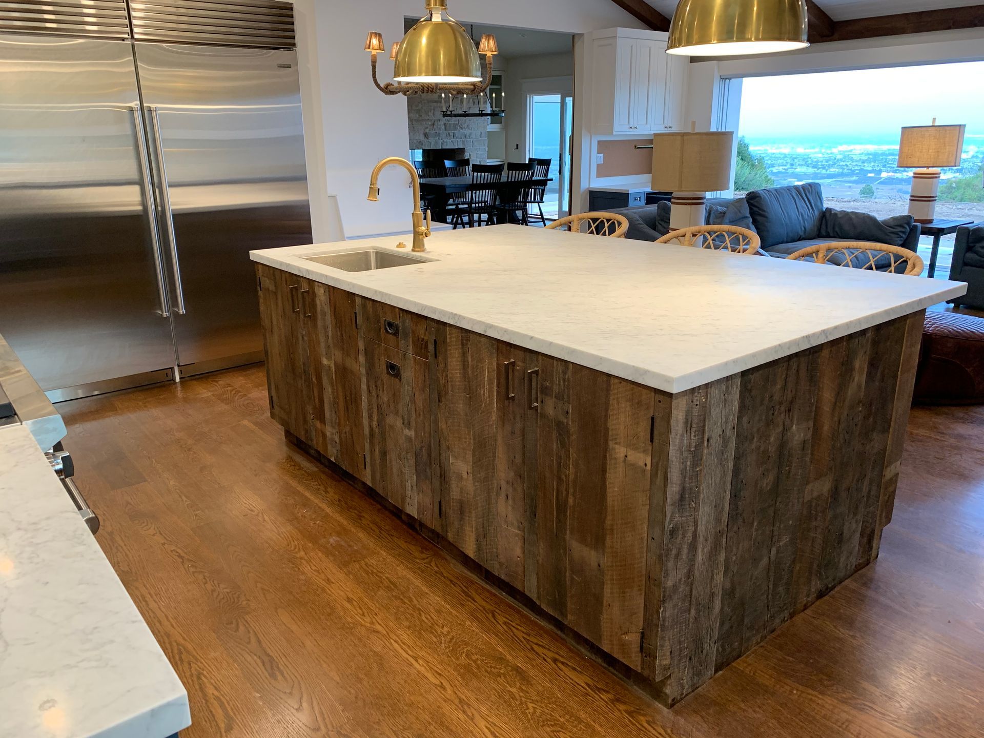 Kitchen island with a light-colored countertop and wooden paneling, golden faucet, and overhead lights.