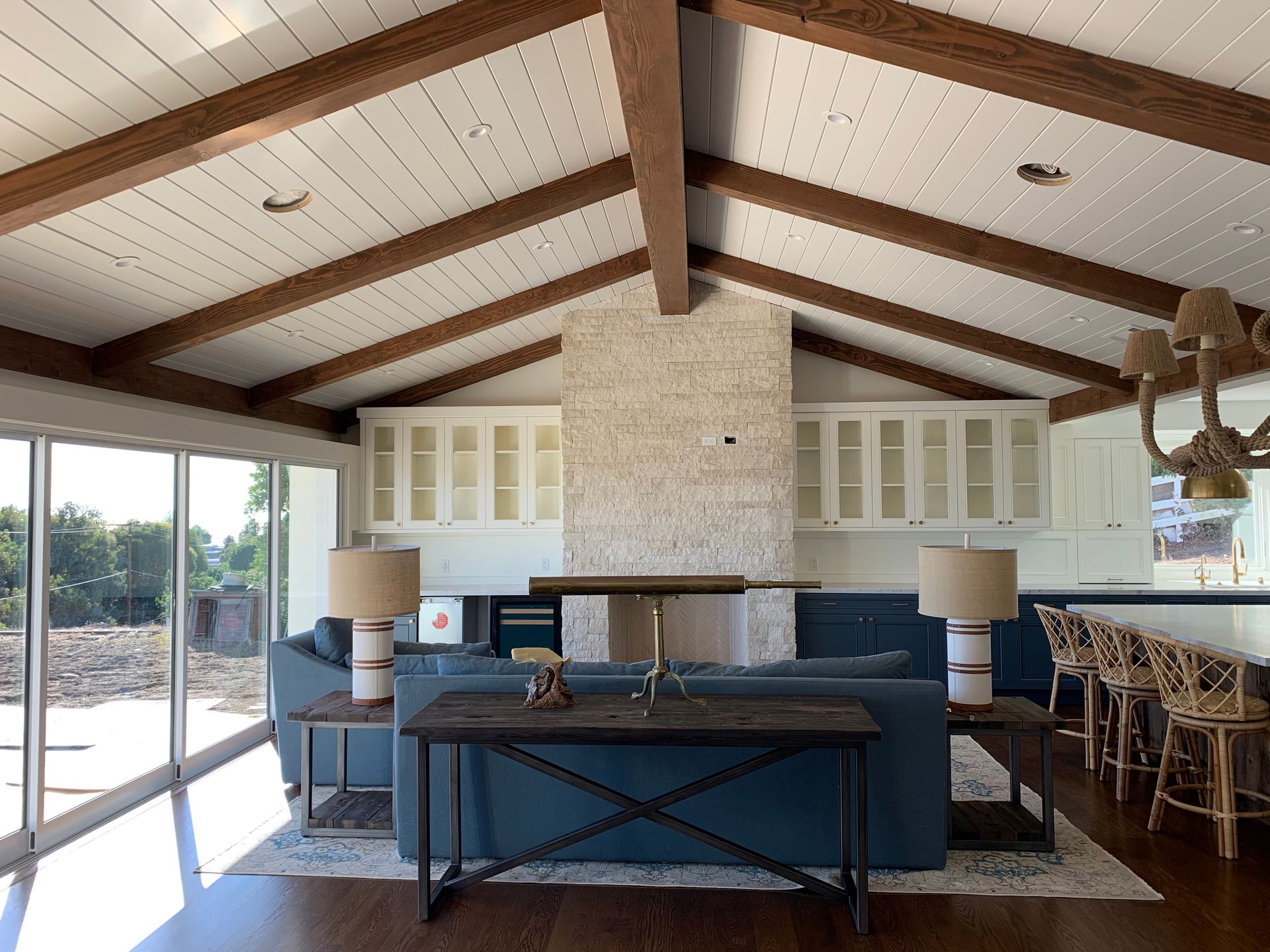 Living room with wood beams, white ceiling, blue sofa, and large windows.