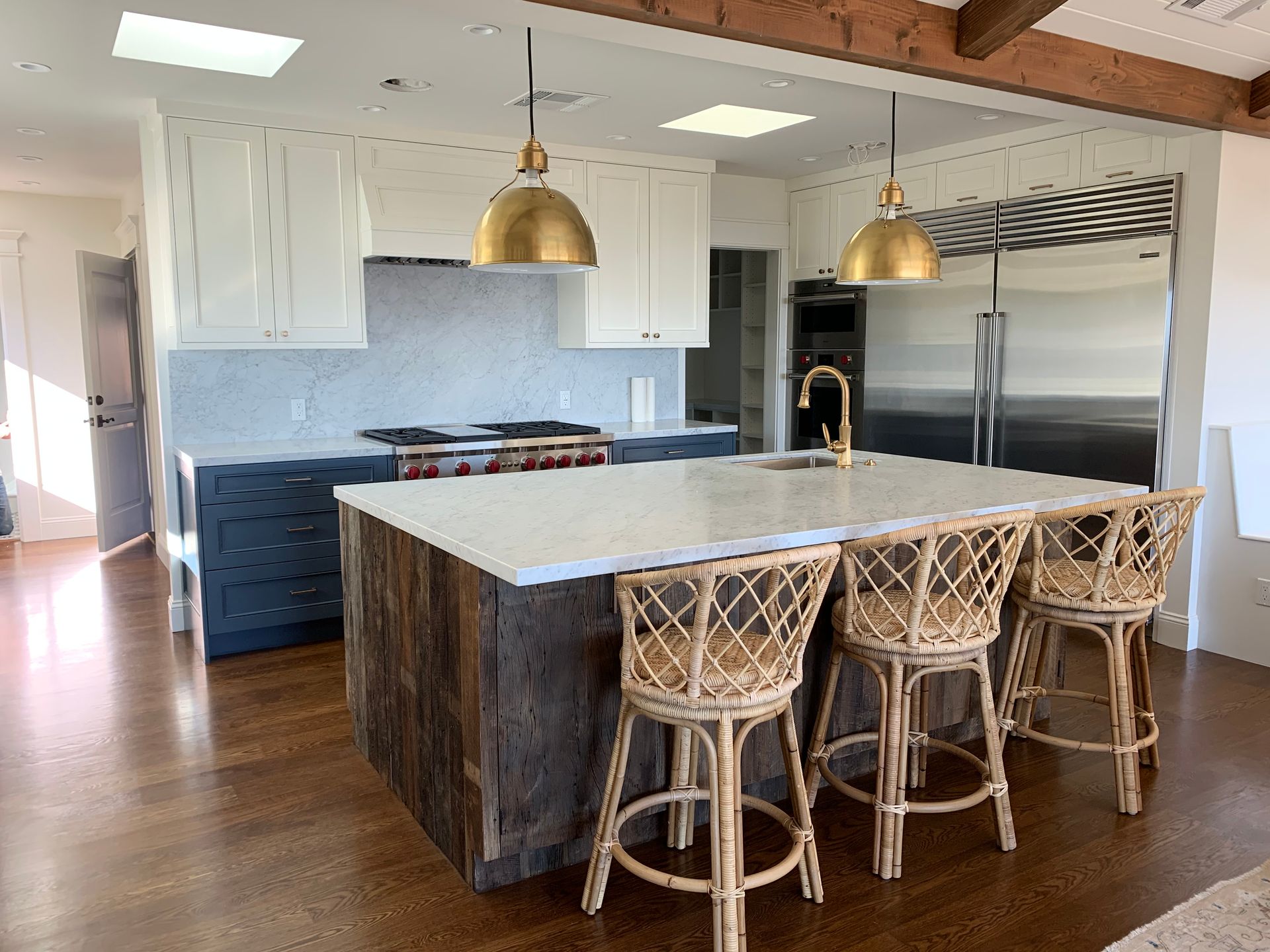 Kitchen with a rustic wooden island, white countertops, blue cabinets, and gold light fixtures.