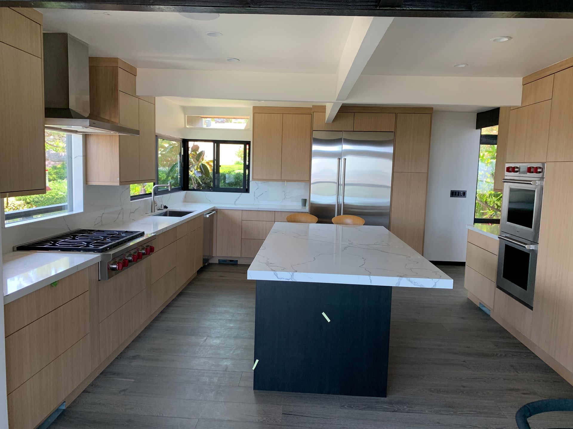 Modern kitchen with light wood cabinets, stainless steel appliances, and a marble-topped island.