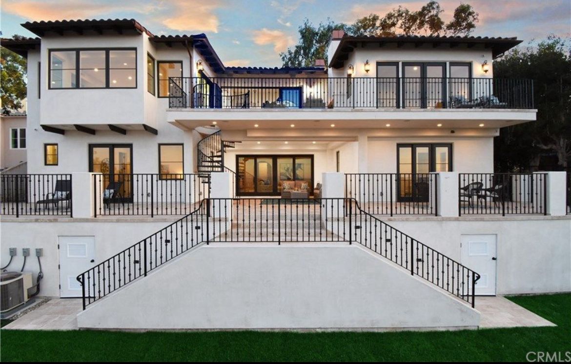 Multi-level white stucco house with black railings and balconies, exterior view.