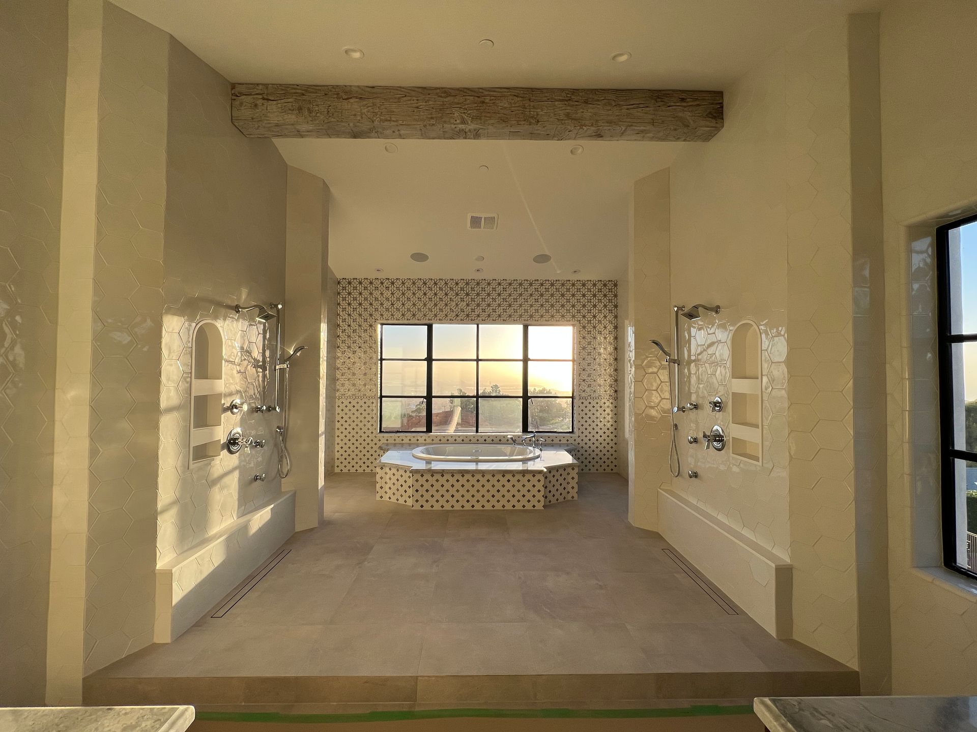 Spacious, modern bathroom with dual showers, large window, and central soaking tub. Neutral tones with tiled accents.