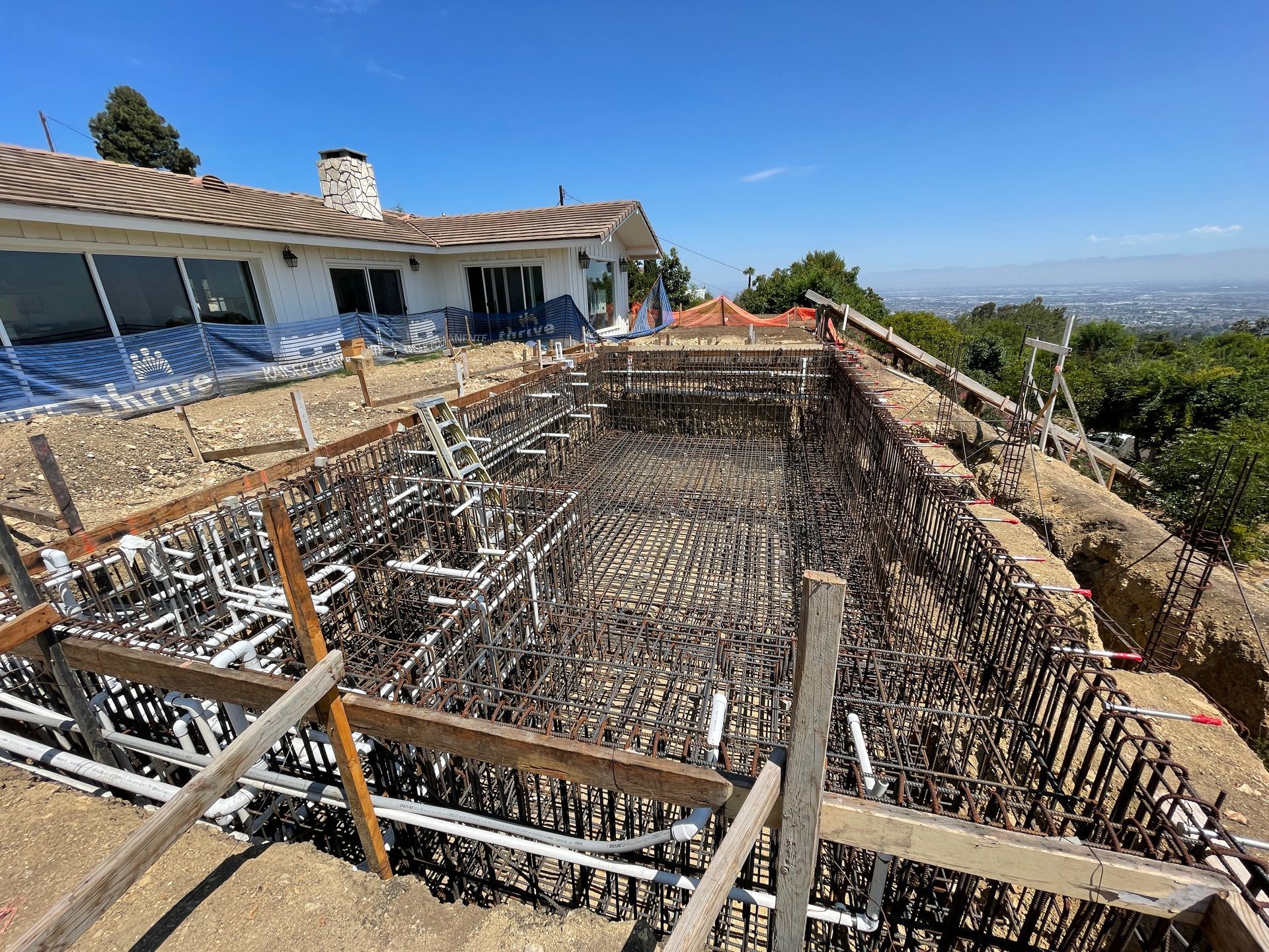 Pool under construction with rebar framework and house in the background. Sunny day, elevated view.