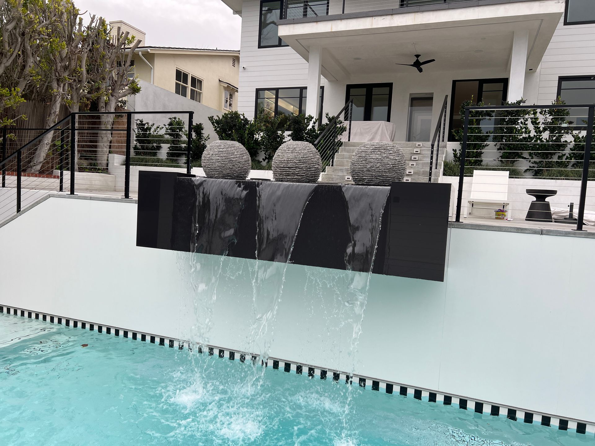 Pool with black waterfall feature, white building, and decorative spheres.