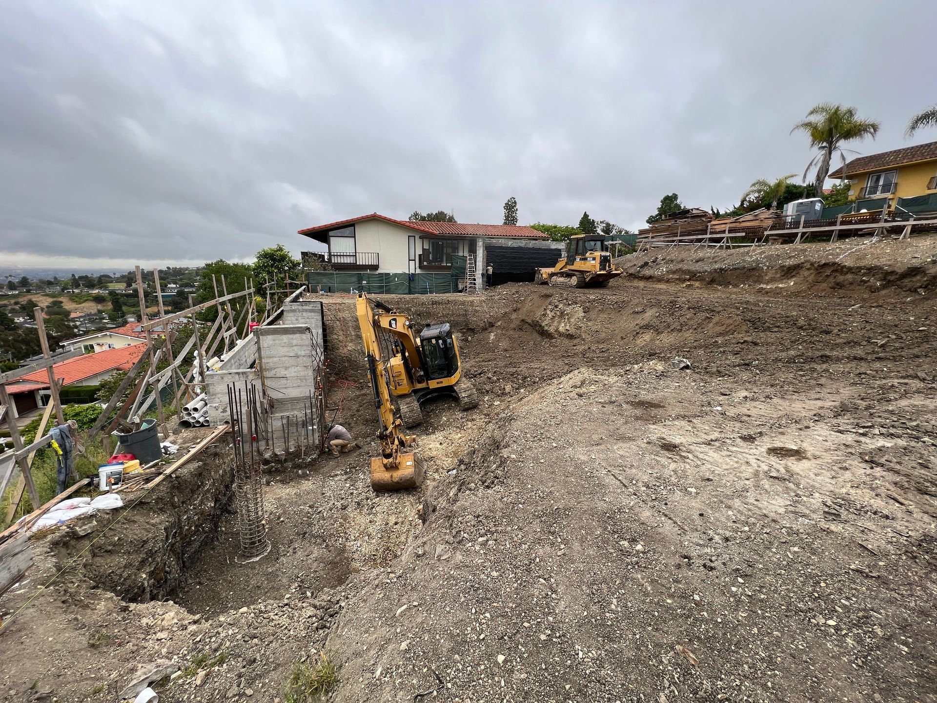 Construction site with excavator and bulldozer on a hillside, cloudy sky.