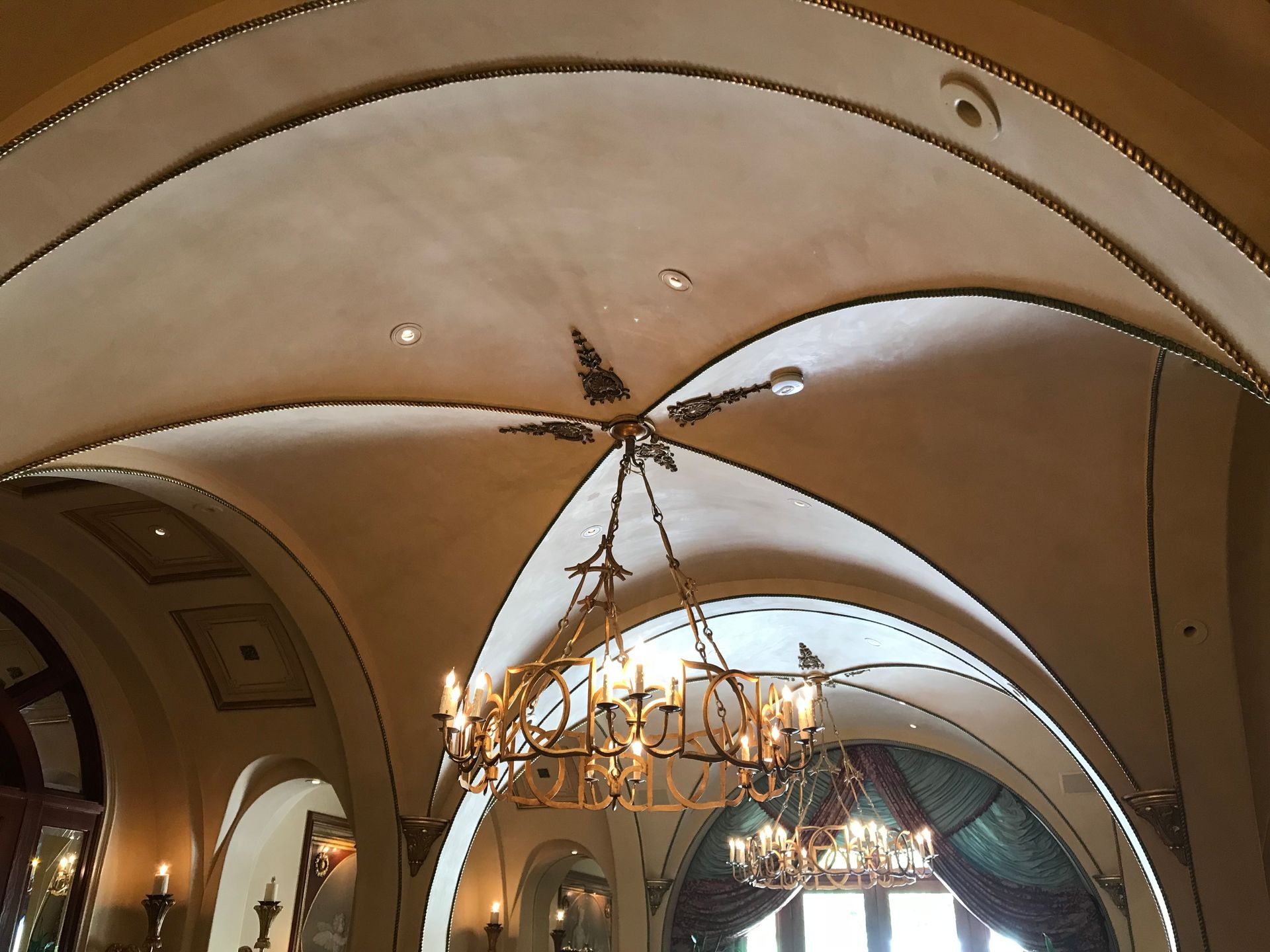 Ornate, arched ceiling with chandeliers. Beige and gold tones, interior of a building.