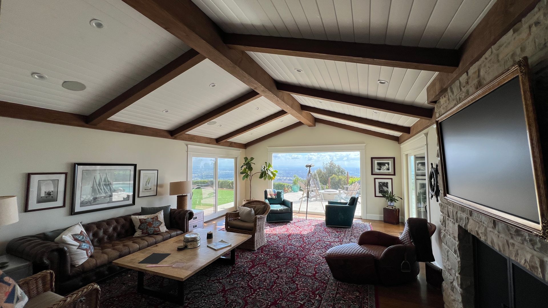 Living room with beamed ceiling, fireplace, and view of landscape. Leather sofa, chairs, rug.