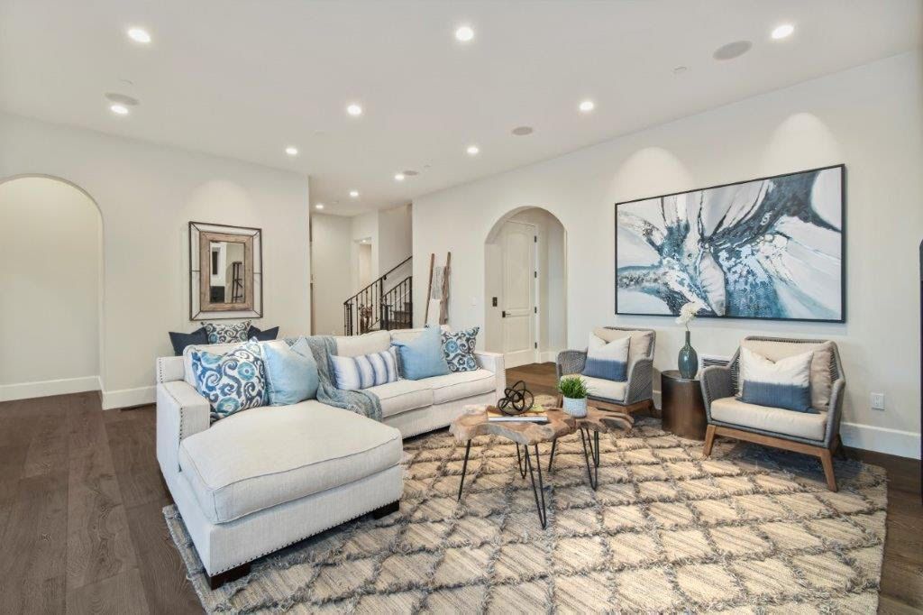 Living room with white walls, sectional sofa, rug, two armchairs, and abstract blue artwork.