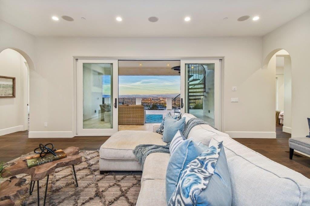 Living room with large sliding doors leading to a balcony with city views. Light-colored couch and rug.