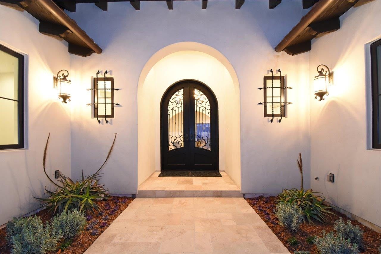 Arched doorway with wrought iron door, flanked by sconces, leading to a home entrance.