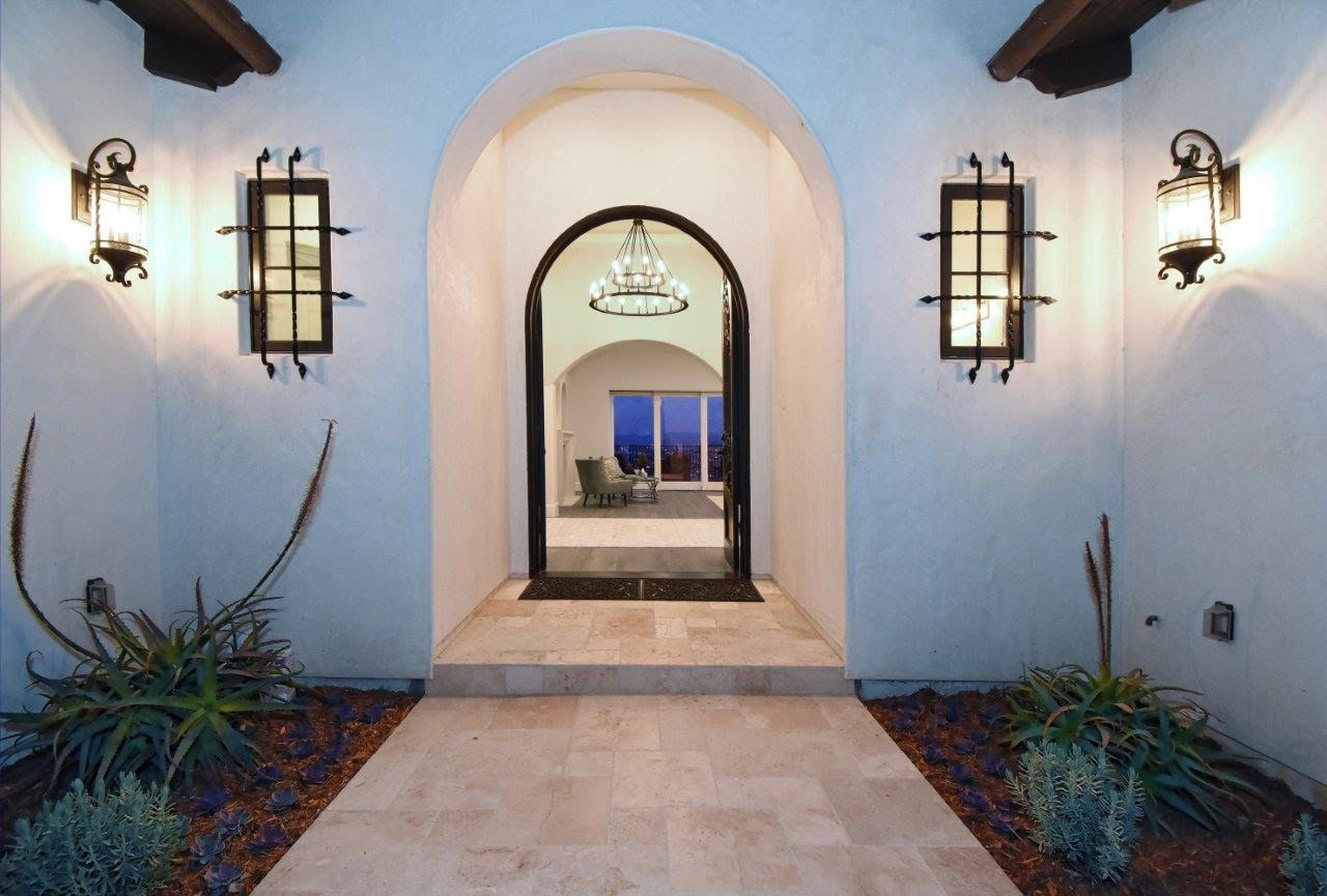 Arched doorway entrance with sconce lighting, leading to a living room with a chandelier and outdoor view.