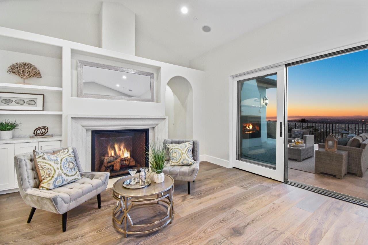 Living room with fireplace, armchairs, and sliding door to a balcony with sunset view.