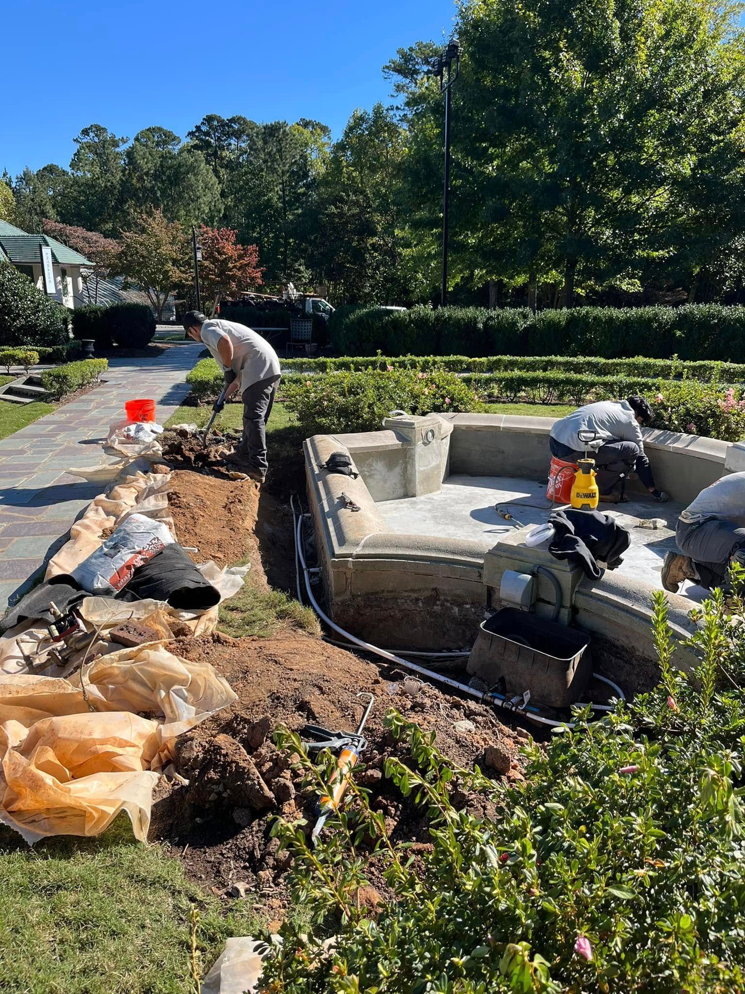A group of people are working on a concrete patio in a garden.