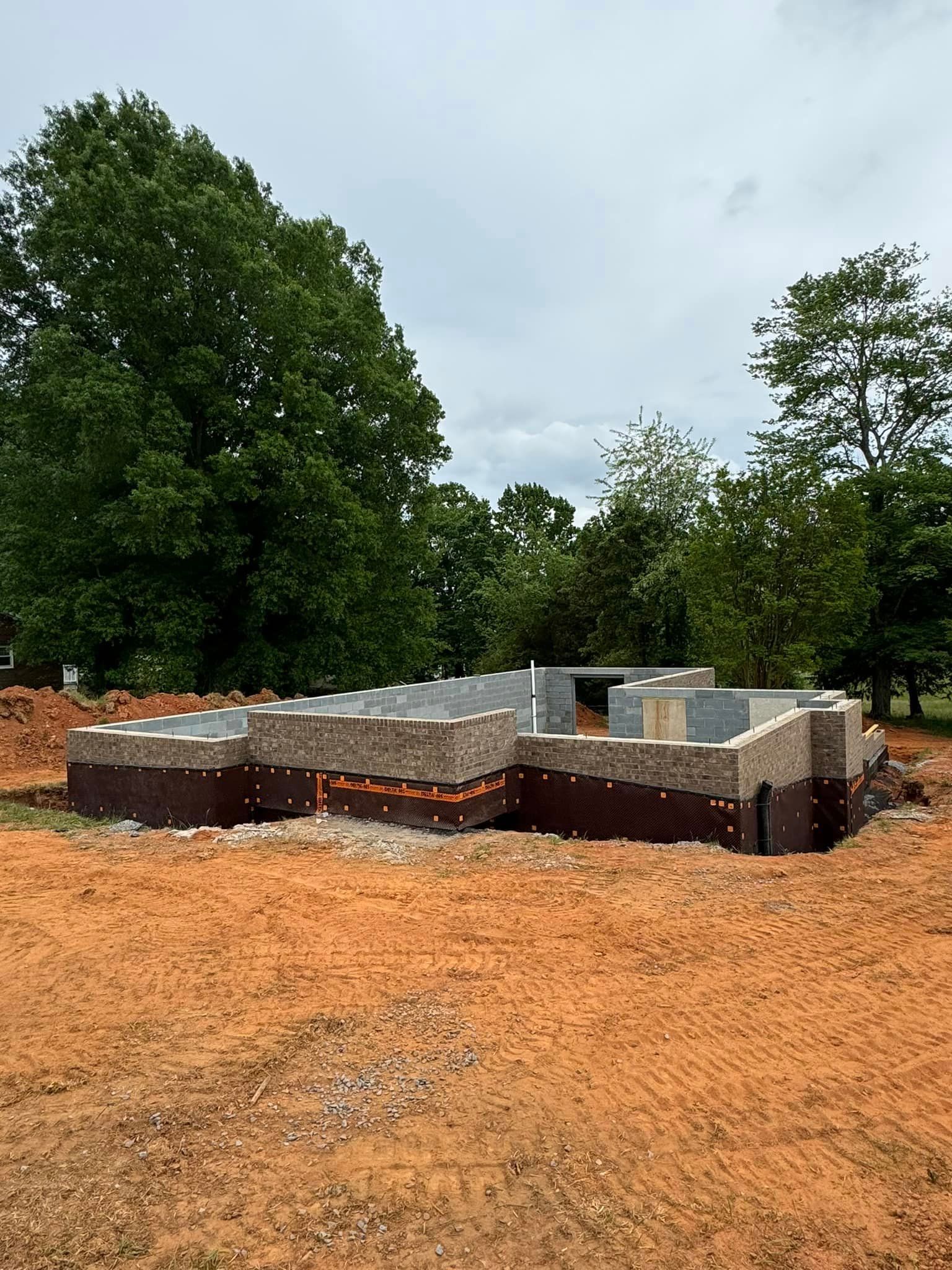 A house is being built in a dirt field with trees in the background.