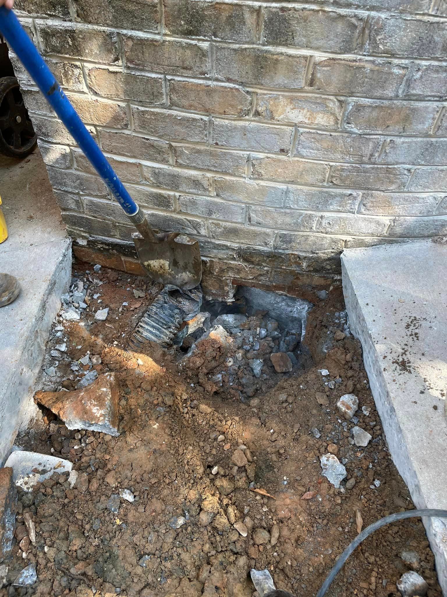 A person is digging a hole in the ground next to a brick wall.