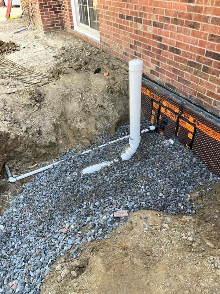 A white pipe is sitting in the dirt next to a brick wall.