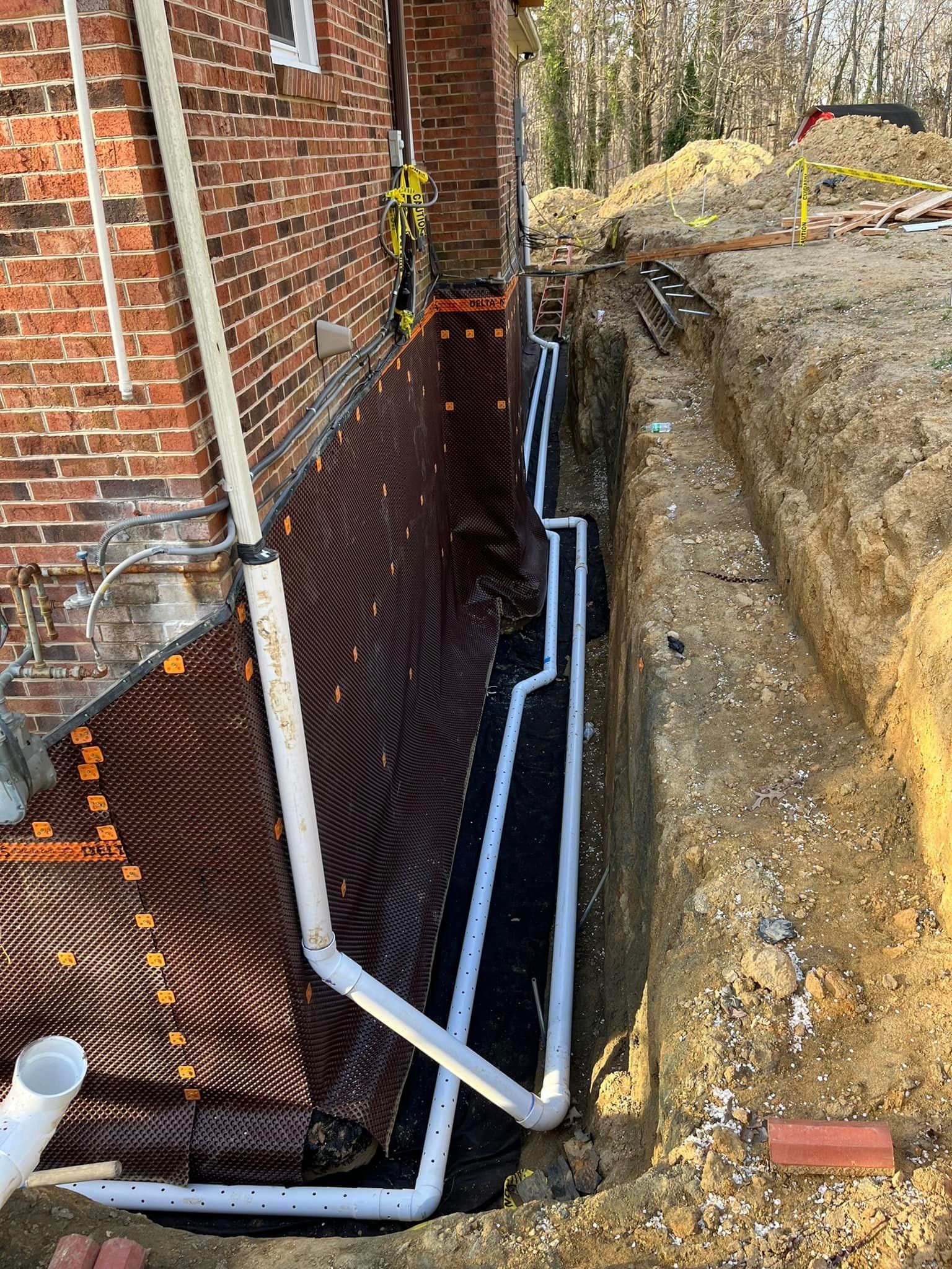 A drainage system is being installed on the side of a brick house.
