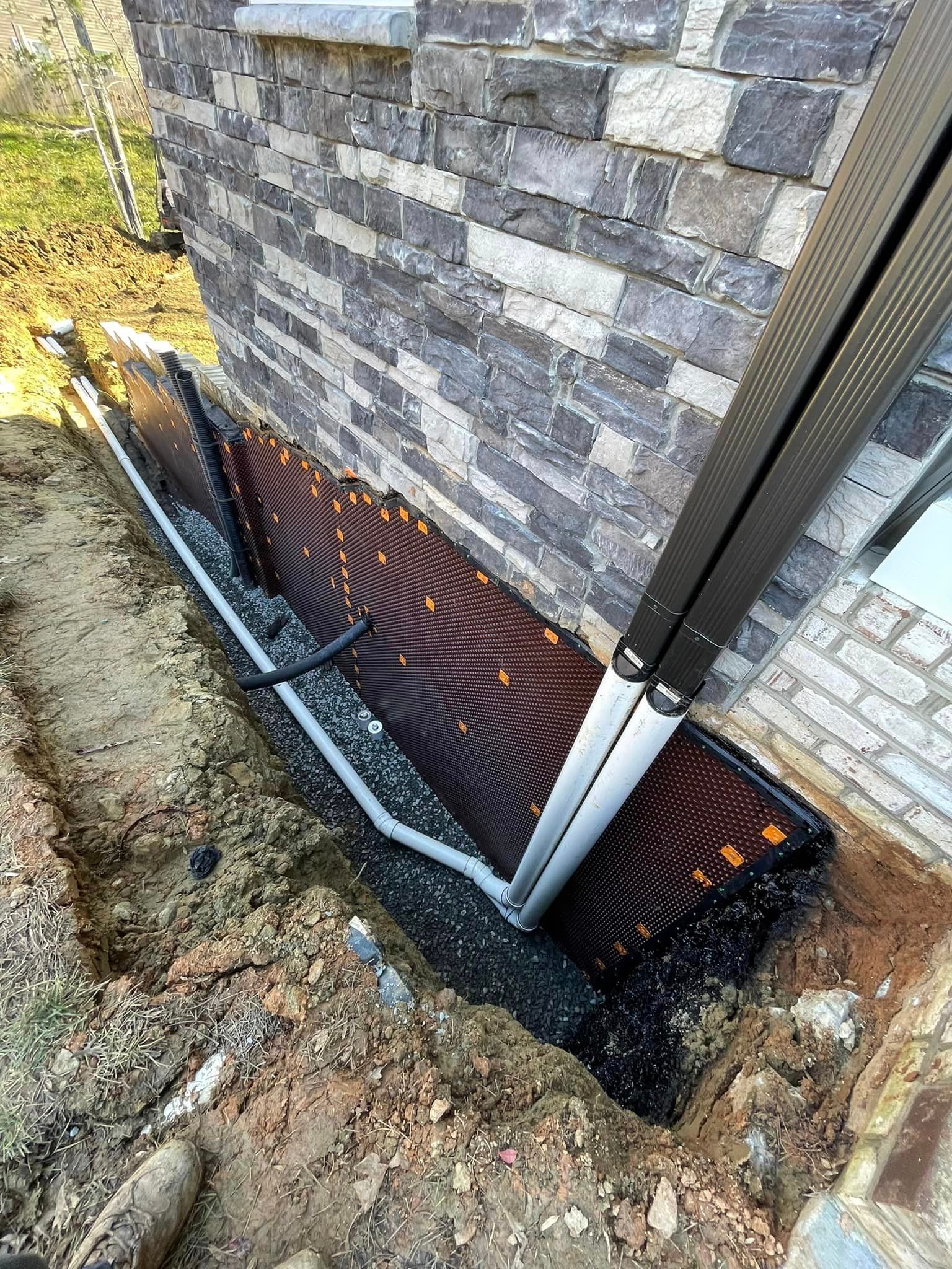 A drainage system is being installed on the side of a brick building.