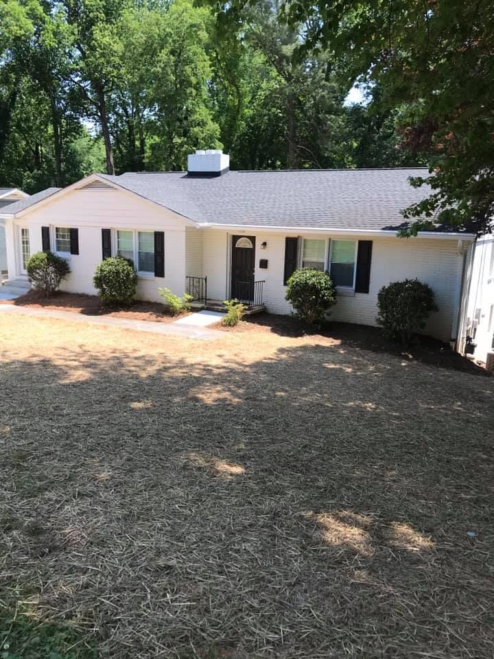 A white house with a brown roof and a large lawn in front of it.