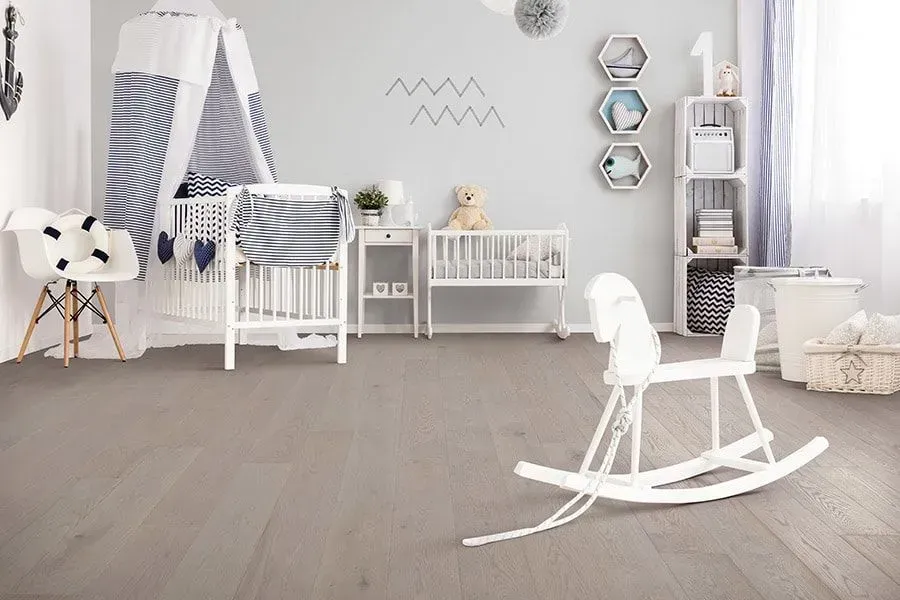Child's room with white cribs, a rocking horse, and gray hardwood floors.